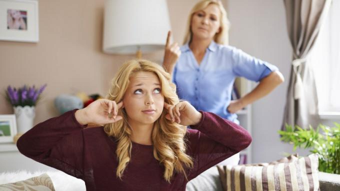 Gadis remaja yang menantang menutupi telinga dengan jari-jari di kamar sementara ibu menegurnya