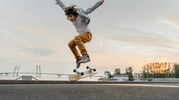 Anak laki-laki melompat dengan skateboard di jalan. Skater anak lucu berlatih ollie di skateboard saat matahari terbenam.